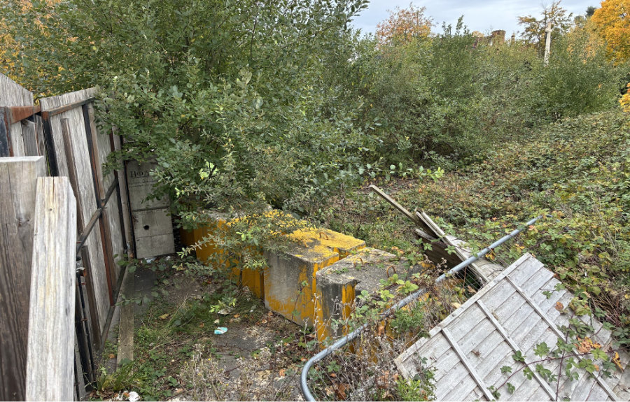 Behind the wooden hoardings, the land remains derelict and overgrown